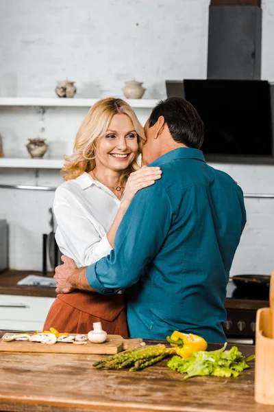 Happy middle aged wife and husband hugging in kitchen — Stock Photo