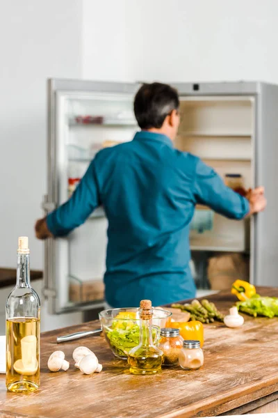 Взгляд сзади зрелого мужчины, смотрящего в холодильник на кухне — стоковое фото