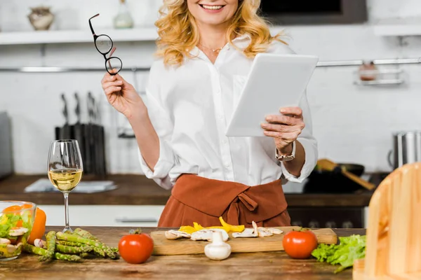 Imagen recortada de la mujer madura sonriente utilizando tableta en la cocina - foto de stock