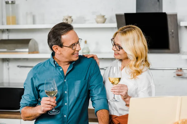 Reife Frau und Mann halten Weingläser in der Hand und schauen einander in der Küche an — Stockfoto