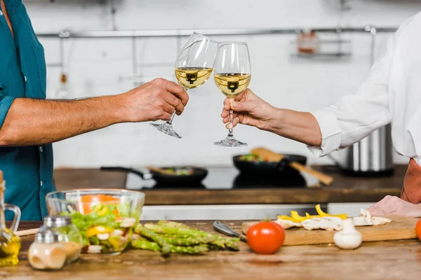 Image recadrée de femme et mari cliquetis avec des verres de vin dans la cuisine — Photo de stock