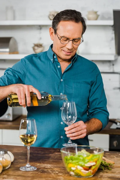 Guapo maduro hombre verter vino en vidrio en la cocina - foto de stock