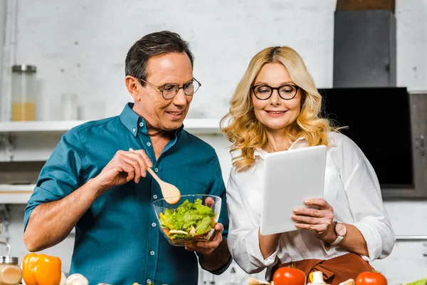 Ältere Frau zeigt Ehemann in Küche etwas auf Tablet — Stockfoto