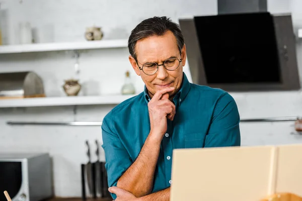 Pensive handsome mature man looking at cookbook in kitchen — Stock Photo