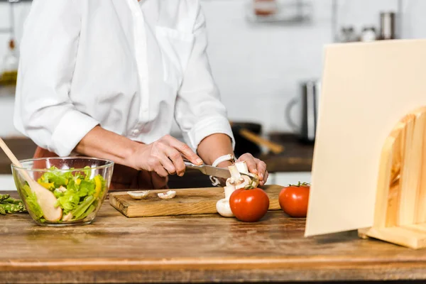 Cropped image of mature woman cutting mushrooms in kitchen — Stock Photo