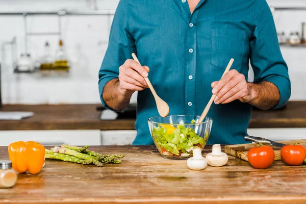 Cropped image of mature man mixing salad in bowl in kitchen — Stock Photo