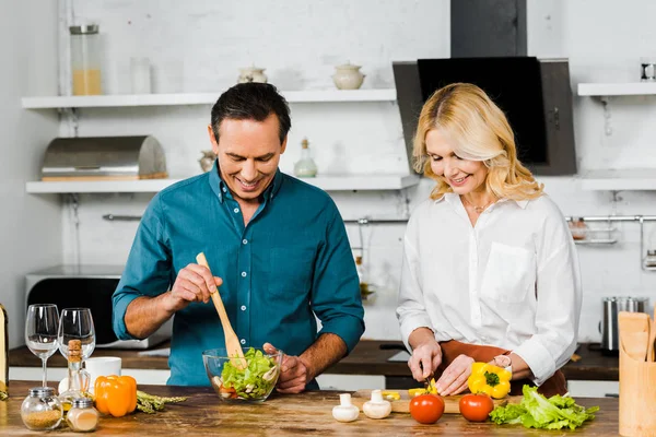 Esposa madura y marido cocinando ensalada orgánica juntos en la cocina - foto de stock