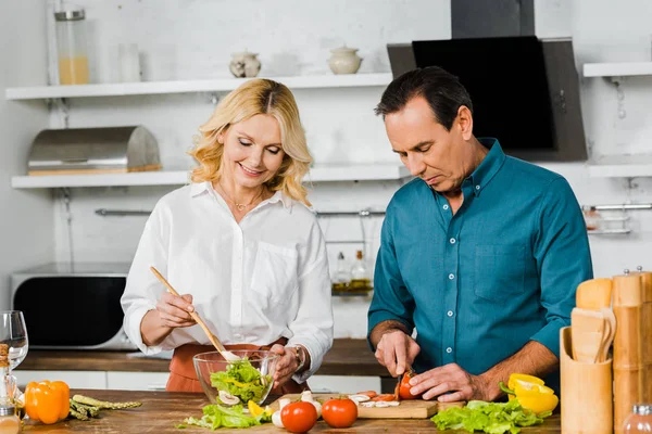 Mature wife and husband cooking delicious salad together in kitchen — Stock Photo