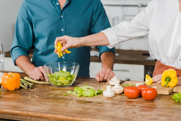 Imagen recortada de la esposa madura y el marido preparando ensalada juntos en la cocina - foto de stock