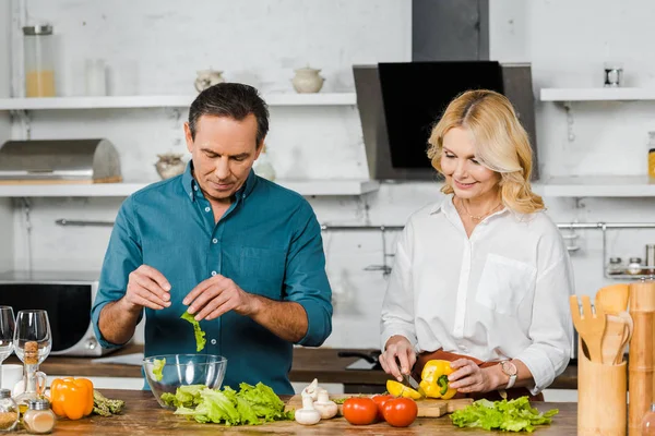 Mature wife and husband cooking salad together in kitchen — Stock Photo