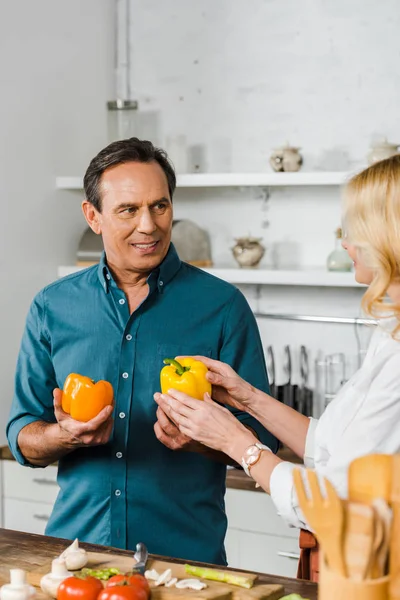 Mature wife and husband holding bell peppers for salad in kitchen — Stock Photo