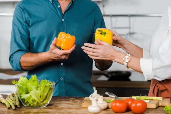 Abgeschnittenes Bild einer reifen Frau, die ihrem Mann Paprika zum Kochen von Salat in der Küche gibt — Stockfoto