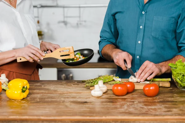 Cropped image of mature wife and husband cooking vegetables in kitchen — Stock Photo