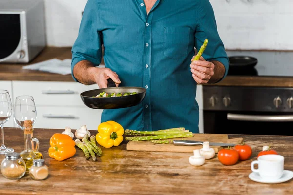 Imagen recortada de hombre de mediana edad cocinar verduras en la sartén en la cocina - foto de stock