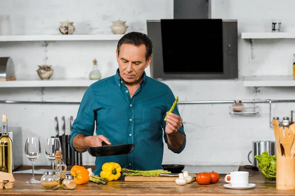 Bell'uomo di mezza età che cucina verdure sulla padella in cucina — Foto stock