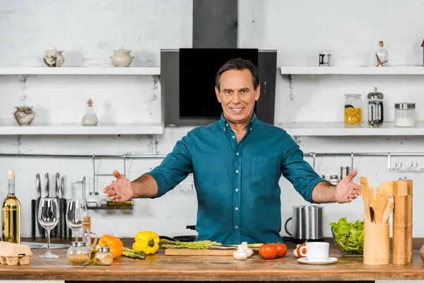 Heureux beau homme d'âge moyen debout avec les bras ouverts et regardant la caméra dans la cuisine — Photo de stock