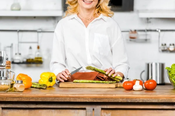 Abgeschnittenes Bild einer lächelnden Frau mittleren Alters, die Gemüse in der Küche schneidet — Stockfoto