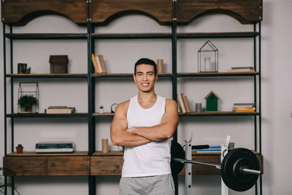 Guapo musculoso bi-racial hombre de pie con brazos cruzados en la sala de estar - foto de stock