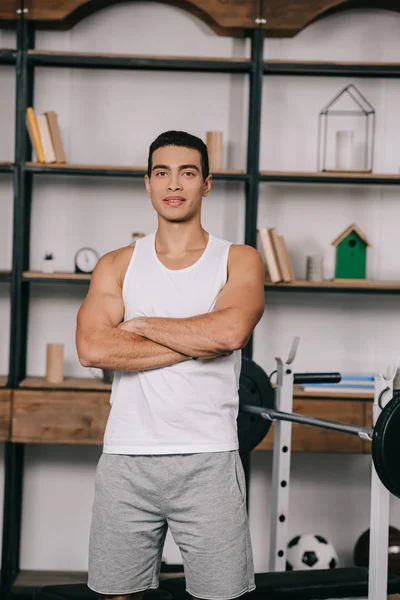 Homme bi-racial musclé debout avec les bras croisés dans le salon — Photo de stock