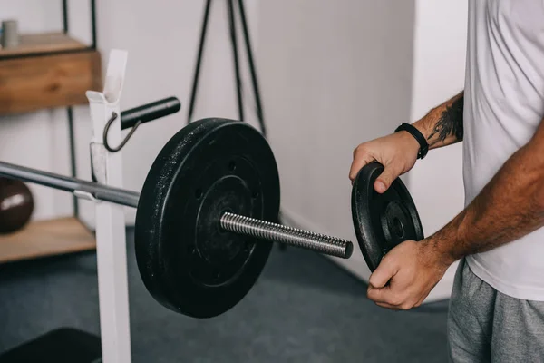 Cropped view of man putting disk on barbell — Stock Photo
