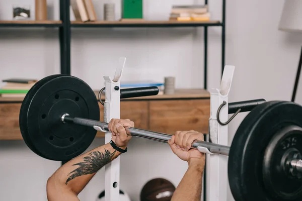 Cropped view of man with tattoo workout with barbell in home gym — Stock Photo
