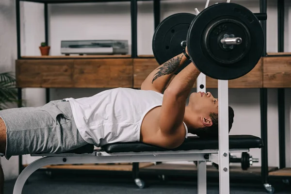 Tatoué mixte homme de course exercice avec haltère dans la salle de gym à domicile — Photo de stock