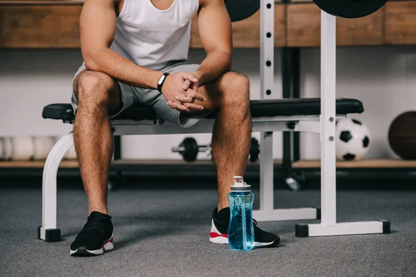 Vista recortada del hombre sentado con reloj de fitness cerca de la botella de deporte - foto de stock