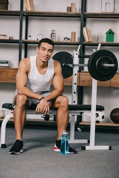 Cheerful muscular mixed race man sitting near sport bottle — Stock Photo