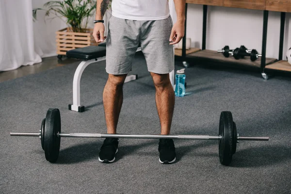 Cropped view of man standing near barbell and sport bottle — Stock Photo