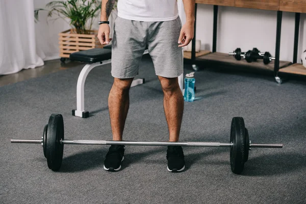 Vue recadrée de l'homme debout près de barbell et bouteille de sport — Photo de stock