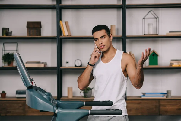 Bi-racial sportsman talking on smartphone near treadmill — Stock Photo