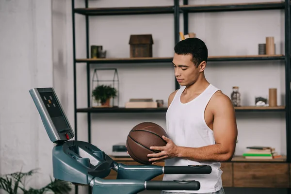 Guapo mixto raza hombre celebración baloncesto cerca de cinta de correr - foto de stock