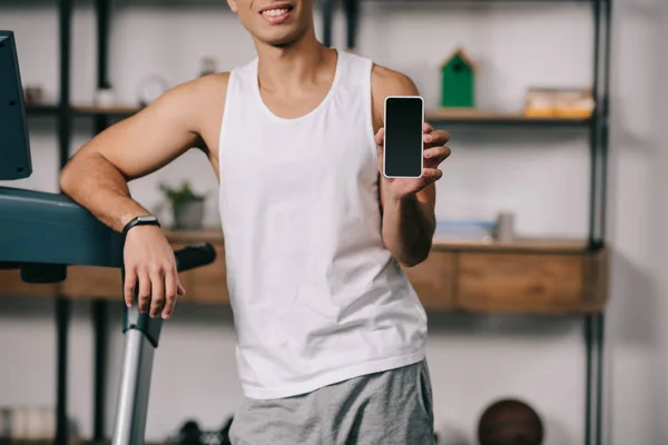 Cropped view of cheerful mixed race man smiling and holding smartphone with blank screen — Stock Photo