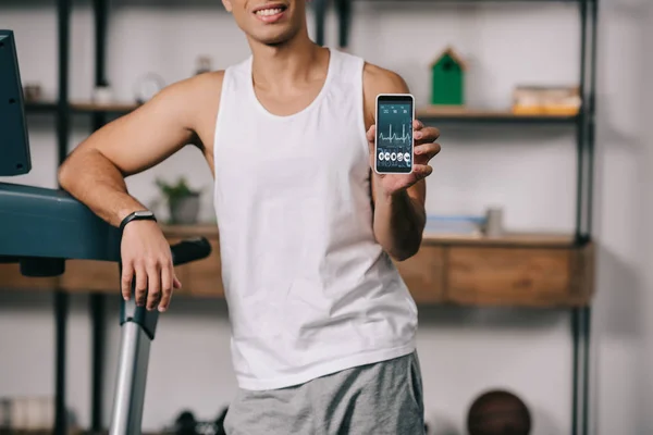 Ausgeschnittene Ansicht eines zweirassigen Mannes, der ein Smartphone mit Herzschlagrate auf dem Bildschirm hält — Stockfoto