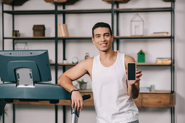 Guapo bi-racial hombre sonriendo y sosteniendo teléfono inteligente con pantalla en blanco - foto de stock