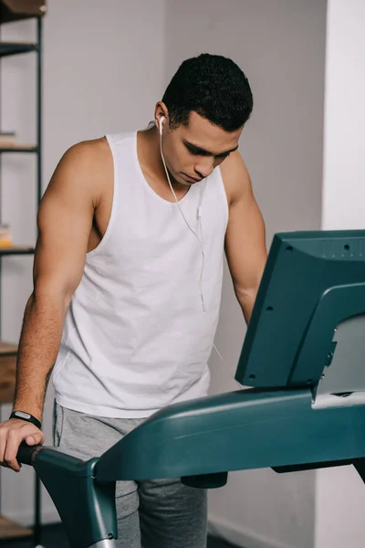 Hombre de raza mixta haciendo ejercicio en la cinta de correr y escuchando música en los auriculares - foto de stock