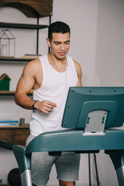 Mixed race man exercising on treadmill and listening music in earphones — Stock Photo