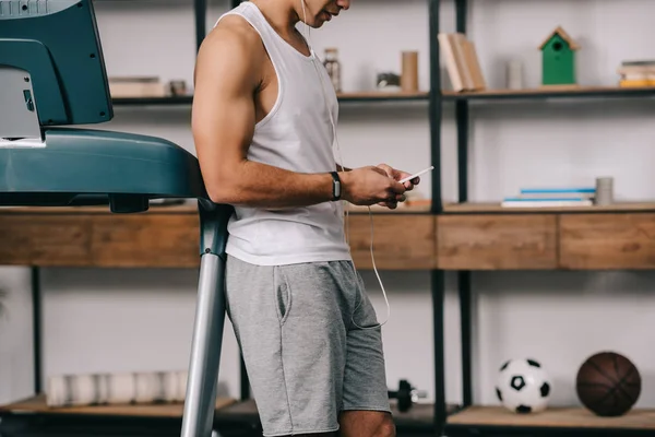 Ausgeschnittener Blick auf einen Mann, der in Sportkleidung steht und Musik in Kopfhörern hört, während er sein Smartphone benutzt — Stockfoto