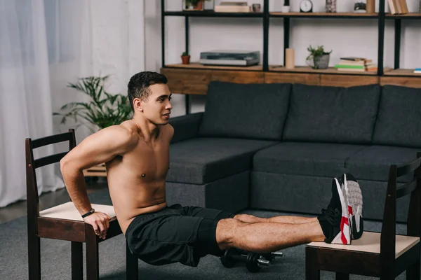 Handsome mixed race man  exercising on chairs in apartment — Stock Photo