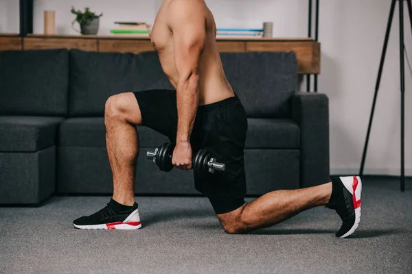 Vue recadrée de l'homme faisant des exercices de fentes avec haltère près du canapé — Photo de stock