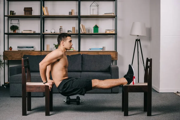 Forte uomo di razza mista che esercita sulle sedie in palestra di casa — Foto stock