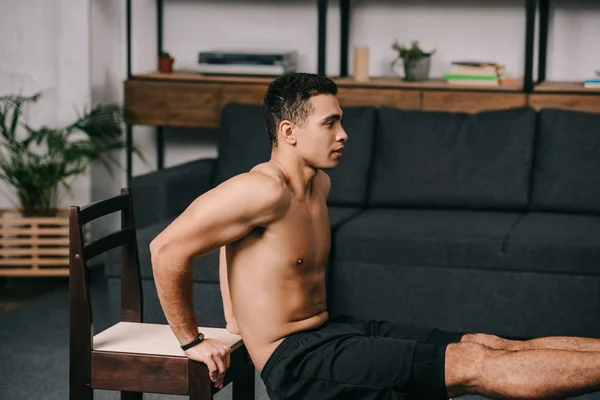 М'язистий змішана раса чоловік займається на стільці у вітальні — стокове фото