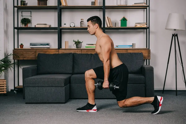 Guapo mixto raza hombre haciendo embestidas ejercicio con pesado dumbbell en casa gimnasio - foto de stock