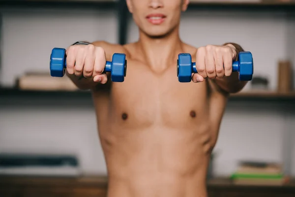 Vista recortada del hombre de raza mixta que hace ejercicio con pesas azules - foto de stock