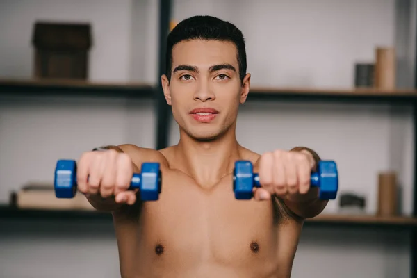 Enfoque selectivo del hombre bi-racial que hace ejercicio con pesas azules - foto de stock