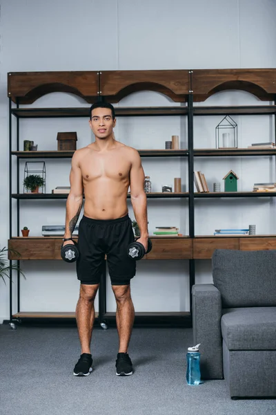 Muscoloso uomo bi-razziale in piedi con pesanti manubri in soggiorno — Foto stock