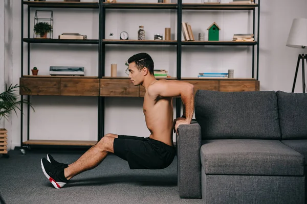 Beau mixte homme séance d'entraînement près du canapé dans le salon — Photo de stock