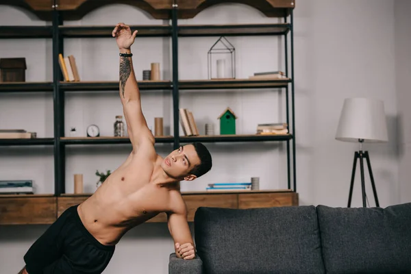 Hombre de raza mixta tatuado haciendo ejercicio de tablón en la sala de estar - foto de stock