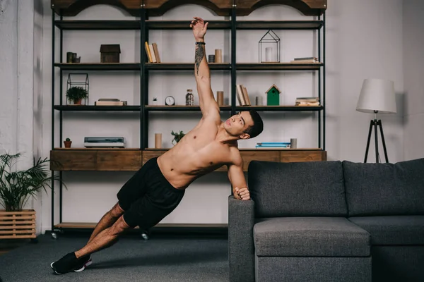 Handsome tattooed mixed race man doing plank exercise in living room — Stock Photo