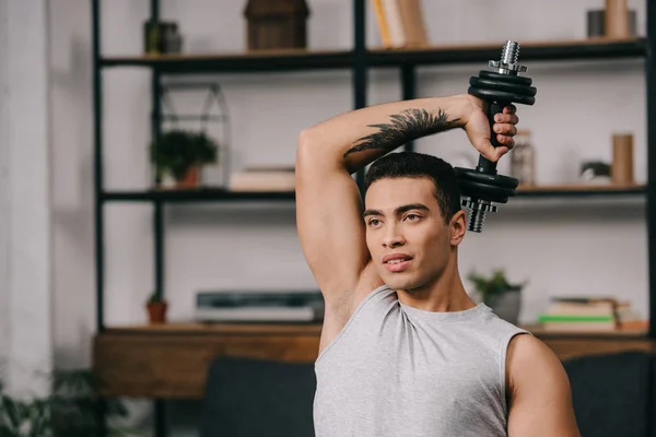 Дворасовий чоловік з татуюванням в руці тримає гантелі над головою — стокове фото
